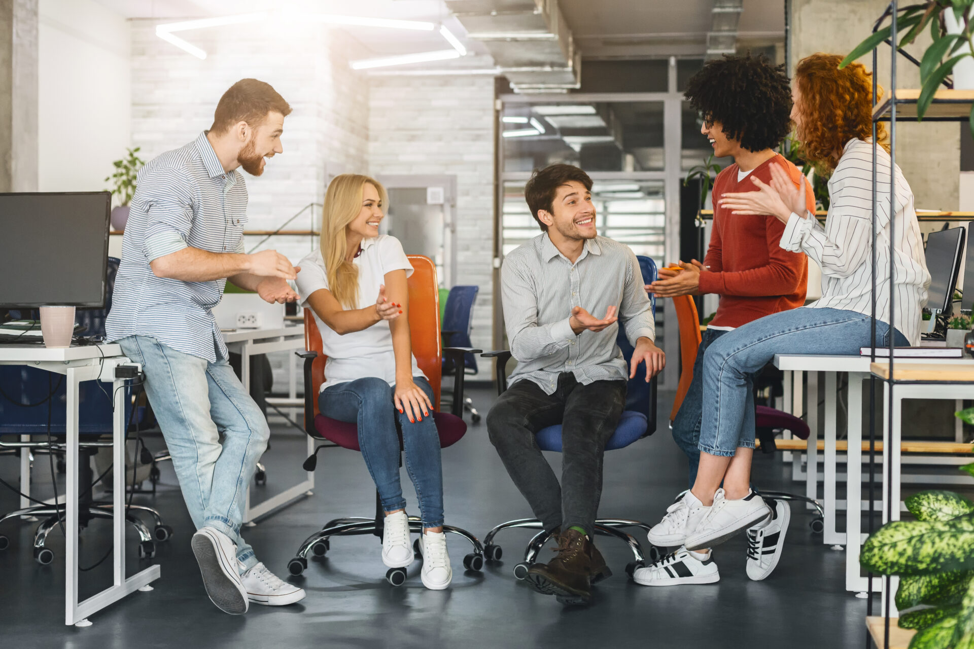 Informal business meeting. Cheerful millennial creative team having pleasant conversation in office